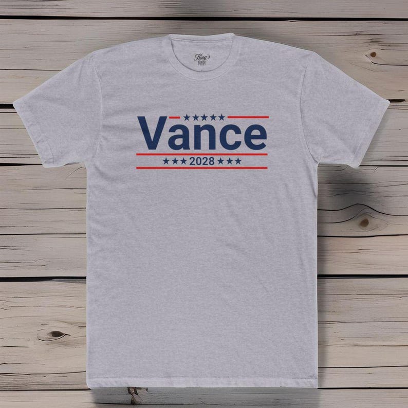 May include: A gray t-shirt with a blue and red design. The design features the word "Vance" in blue with red stars and stripes above and below the word. The text "2028" is also included in the design.