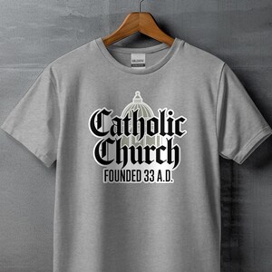 May include: Gray t-shirt with a black graphic of a church building and the text "Catholic Church Founded 33 A.D."