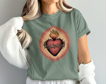 Könnte beinhalten: Salbeigrünes T-Shirt mit einer detaillierten Grafik eines Herzens, das von einer Dornenkrone, Flammen und einem strahlenden Hintergrund umgeben ist. Das Design ist auf dem T-Shirt zentriert und bietet eine Vintage-Ästhetik.