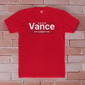 May include: Red t-shirt with white text that says "Vance 2028" with stars above and below the text.