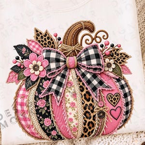 May include: An ivory t-shirt featuring a large, decorative pumpkin graphic. The pumpkin is composed of various patterned fabric segments in pink, black, and white, including leopard print, gingham, and floral designs, accented with a plaid bow.