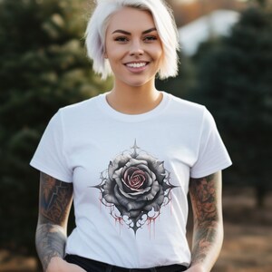 May include: White t-shirt featuring a black and grey rose graphic with red dripping accents. The rose is surrounded by a black and grey intricate design.