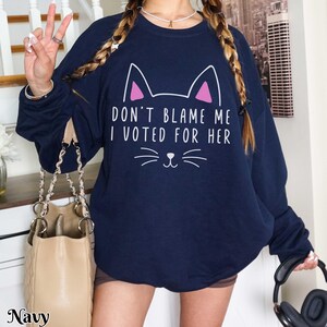 May include: Navy blue sweatshirt with a white cat graphic and the text "Don't blame me I voted for her".