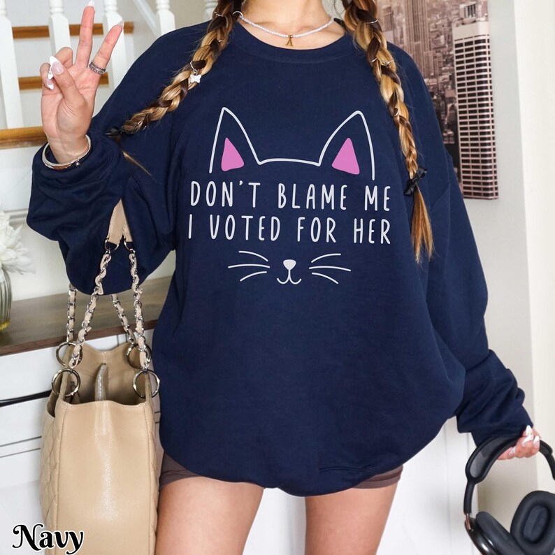 May include: Navy blue sweatshirt with a white cat graphic and the text "Don't blame me I voted for her".