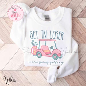 Puede incluir: Sudadera blanca con la frase "GET IN LOSER" sobre una ilustraci&oacute;n de un carrito de golf rosa. Debajo, el texto dice "we're going golfing". La sudadera tiene mangas largas y cuello redondo.