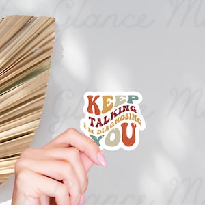 May include: A white sticker with the text "Keep Talking I'm Diagnosing You" in a retro font with colorful letters. The letters are in shades of red, orange, yellow, green, and blue.