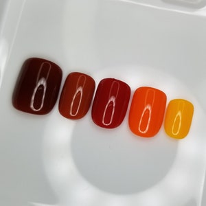 May include: A set of six false nails with a gradient of red, orange, and yellow.