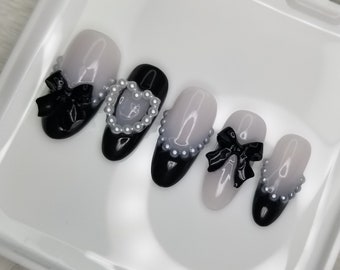 May include: Set of five false nails with a black and white ombre design. Each nail is decorated with a black bow and a pearl accent.