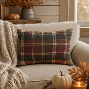 Peut inclure: Un coussin rectangulaire orné d'un motif à carreaux dans des tons de vert foncé, rouge profond et beige. Le tissu présente une texture douce et mate, et le design se compose de lignes horizontales et verticales formant un motif à grille.