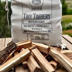 May include: A white canvas bag filled with small pieces of kiln-dried wild black cherry wood. The bag has a black label that reads "Sawed After Tiny Timbers Wild Black Cherry Kiln Crafted Premium Quality Sustainably Sourced in the USA".