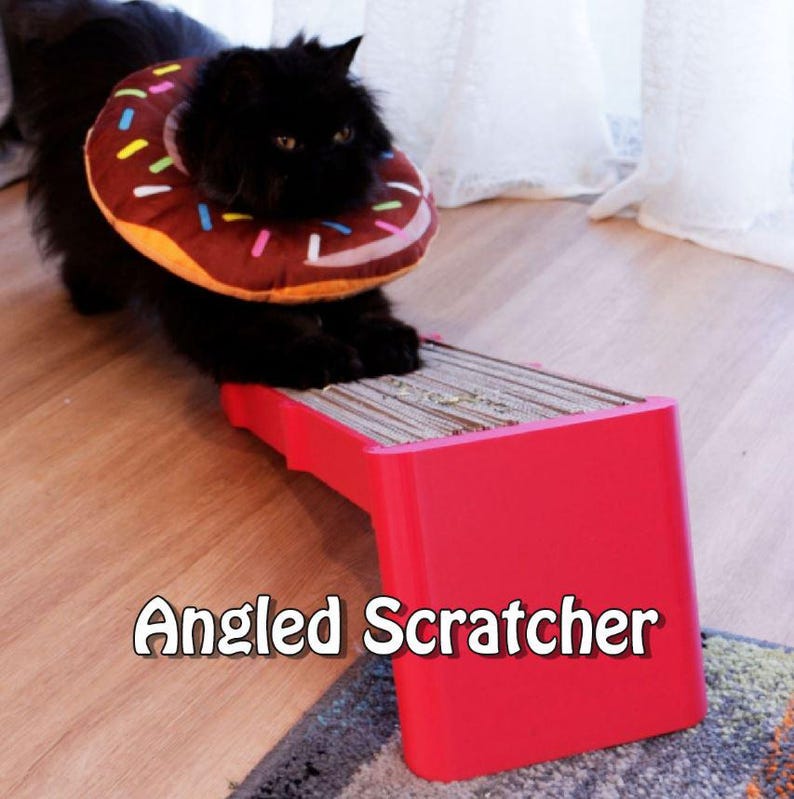 May include: A black cat wearing a donut-shaped recovery collar stands on a red angled cat scratcher. The scratcher has a cardboard scratching surface. The text "Angled Scratcher" is displayed on the red base.
