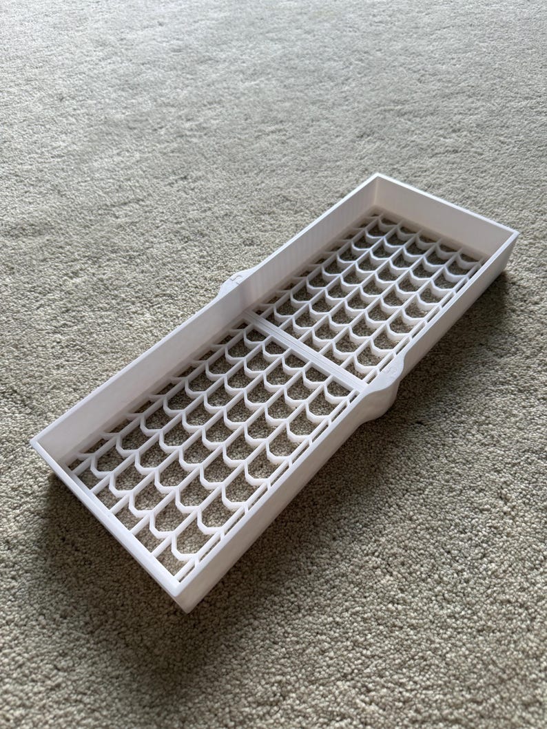 May include: A white rectangular tray with a patterned grid design. The tray has a series of interconnected, curved shapes forming the grid. The tray is made of a solid, opaque white material and is designed to hold small items.