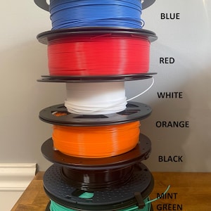 May include: A stack of six spools of filament for 3D printing. The spools are arranged from top to bottom in the following colors: blue, red, white, orange, black, and mint green.