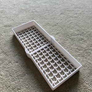 May include: A white, rectangular tray with a grid-like pattern of interconnected, curved shapes. The tray is open and appears to be made of plastic. The design suggests it could be used for organizing small items or as a drying rack.