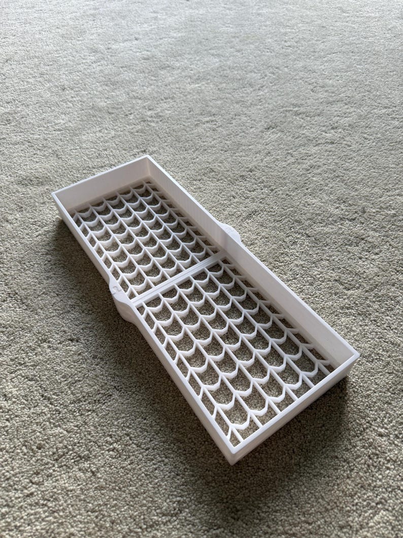 May include: A white, rectangular tray with a grid-like pattern of interconnected, curved shapes. The tray is open and appears to be made of plastic. The design suggests it could be used for organizing small items or as a drying rack.