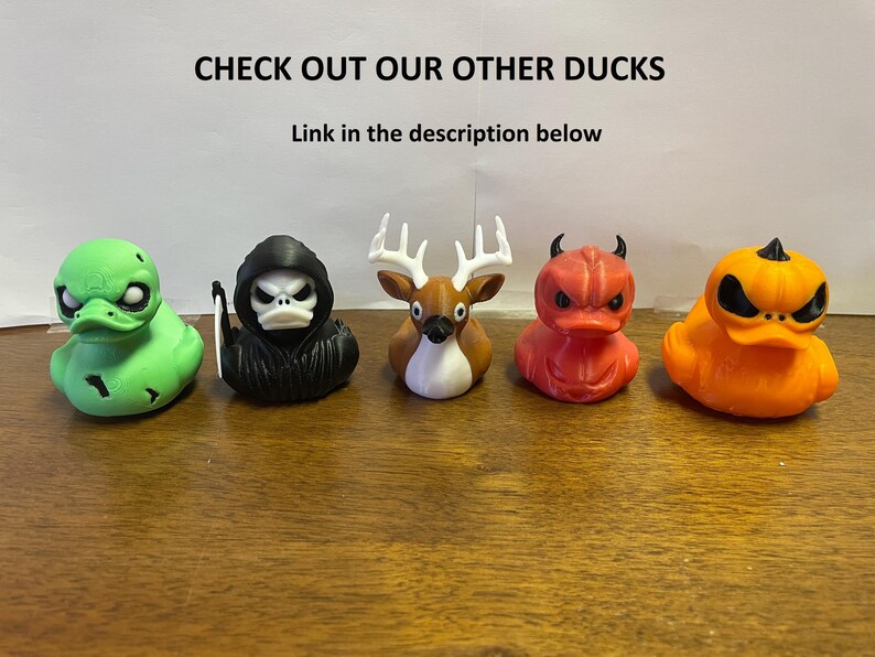May include: Five rubber duck toys with different Halloween themes. The ducks are green, black, brown, red, and orange. The ducks are all facing forward and have different expressions on their faces. The text "CHECK OUT OUR OTHER DUCKS" is at the top of the image. The text "Link in the description below" is below the first line of text.