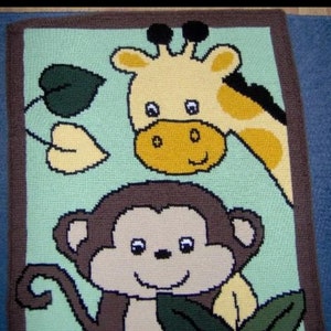 Op de afbeelding: Een kleurrijk gebreid babydekentje met een bruine aap en een gele giraffe. Het dekentje heeft een lichtblauwe achtergrond met groene bladeren.