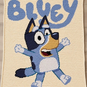 Pode incluir: Uma manta de croch&ecirc; com a personagem Bluey. A manta tem um fundo creme com a palavra "BLUEY" em azul claro. Bluey &eacute; retratado em tons de azul, branco e bege, com uma express&atilde;o de boca aberta, ideal para o quarto das crian&ccedil;as.