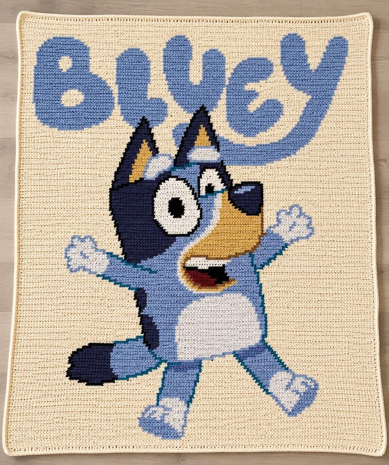 Pode incluir: Uma manta de croch&ecirc; com a personagem Bluey. A manta tem um fundo creme com a palavra "BLUEY" em azul claro. Bluey &eacute; retratado em tons de azul, branco e bege, com uma express&atilde;o de boca aberta, ideal para o quarto das crian&ccedil;as.