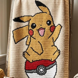 May include: A rectangular crochet blanket featuring a yellow Pikachu character with black-tipped ears, red cheeks, and a pink tongue, sitting atop a red, white, and gray Poké Ball. The blanket has a cream-colored background and a textured border.