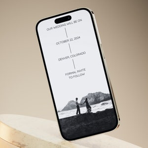 Puede incluir: La pantalla de un tel&eacute;fono inteligente muestra un anuncio de boda. El texto dice "Nuestra boda ser&aacute; el 22 de octubre de 2024 en Denver, Colorado. Invitaci&oacute;n formal a seguir". Una foto en blanco y negro de una pareja de pie en una playa est&aacute; en el fondo.