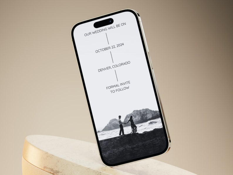 Puede incluir: La pantalla de un tel&eacute;fono inteligente muestra un anuncio de boda. El texto dice "Nuestra boda ser&aacute; el 22 de octubre de 2024 en Denver, Colorado. Invitaci&oacute;n formal a seguir". Una foto en blanco y negro de una pareja de pie en una playa est&aacute; en el fondo.