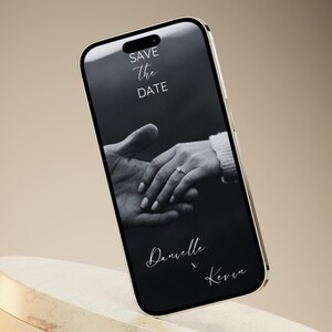 Puede incluir: Una foto en blanco y negro de las manos de una pareja con un anillo en el dedo de la mujer. La foto se muestra en la pantalla de un tel&eacute;fono inteligente con el texto "Save the Date" y "Danielle & Kevin" en la pantalla.