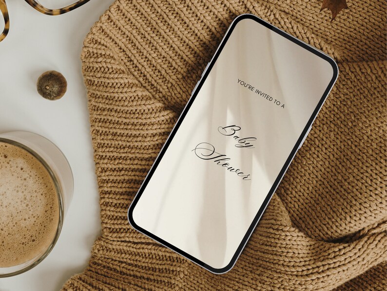 May include: A smartphone displaying a digital invitation to a baby shower. The invitation reads "You're invited to a Baby Shower". The phone is lying on a brown knitted sweater.