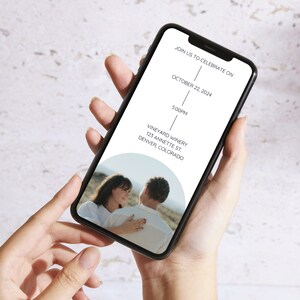 May include: A mobile phone screen displaying a wedding invitation. The invitation is for a wedding on October 22, 2024, at 5:00 PM at Vineyard Winery in Denver, Colorado. A photo of a couple is in the background.