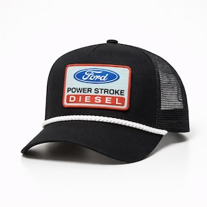 May include: Black trucker hat with a mesh back and a curved brim. The front features a rectangular patch with the Ford logo and the words "POWER STROKE DIESEL". A white rope detail accents the brim.