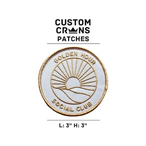 May include: A white embroidered patch with gold thread depicting a stylized sun rising over a horizon with the text "Golden Hour Social Club" around the sun. The patch is 3 inches wide and 3 inches tall.