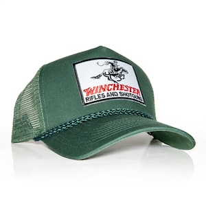 May include: A green trucker hat with a white patch featuring a black and white illustration of a cowboy riding a horse. The patch has the text "Winchester Rifles and Shotguns" in red letters.