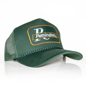 May include: A green trucker hat with a brown and gold patch that says "Remington" in white lettering.
