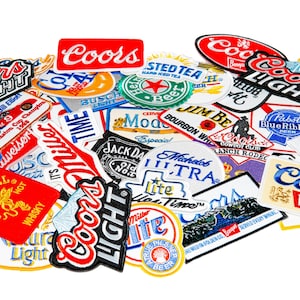 May include: A collection of colorful embroidered patches featuring various beer brands, including Coors Light, Miller Lite, Budweiser, and Pabst Blue Ribbon. The patches are arranged in a random pattern and are all in good condition.