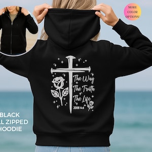 May include: Black full-zip hoodie with a white cross, rose, and text that reads "The Way, The Truth, The Life, John 14:6." The hoodie has a hood and a front zipper. The image also shows a smaller image of the hoodie being worn.