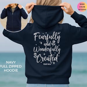 Könnte beinhalten: Marineblauer Kapuzenpullover mit durchgehendem Reißverschluss und dem weißen Text "Fearfully and Wonderfully Created" sowie Psalm 139:14. Der Hoodie hat eine Kapuze mit Kordelzug und eine Vordertasche. Das Bild zeigt auch ein kleineres Bild des getragenen Hoodies.