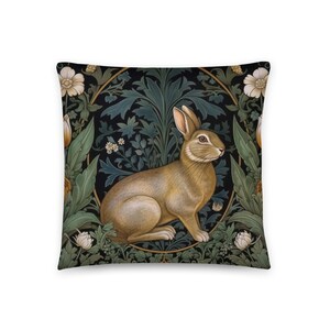 May include: A decorative throw pillow featuring a brown rabbit sitting in a green and gold floral design. The rabbit is surrounded by leaves and flowers, and the background is a dark green.