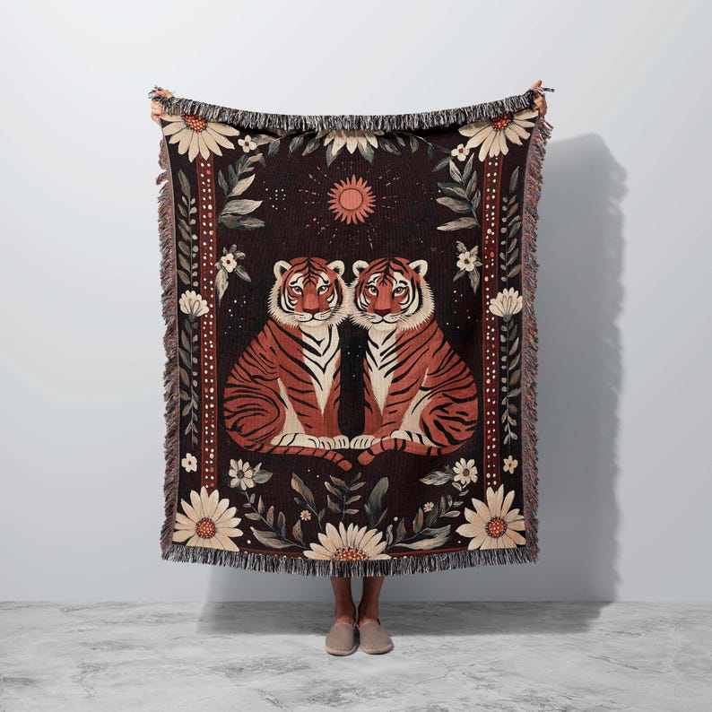 K&ouml;nnte beinhalten: Eine gewebte Wandteppich-Decke mit dunklem Hintergrund, auf der zwei orangefarbene Tiger nebeneinander sitzen. Die Tiger sind von floralen Mustern und einer Sonne in der oberen Mitte der Decke umgeben.