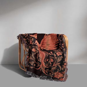 May include: A black and orange woven throw blanket with a floral and bird design. The blanket is draped over a wicker chair.