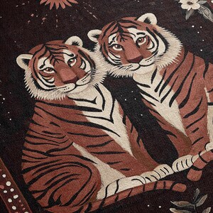 K&ouml;nnte beinhalten: Zwei braune und wei&szlig;e Tiger mit schwarzen Streifen sitzen auf einem dunklen Hintergrund mit einem floralen Muster zusammen. Eine kleine Sonne mit orangefarbenen Strahlen befindet sich in der oberen linken Ecke des Bildes.