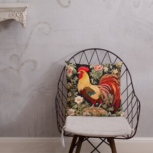 May include: A throw pillow with a colorful rooster design on a black background. The rooster is surrounded by flowers and leaves. The pillow is sitting on a chair.