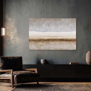 May include: An abstract landscape painting in neutral tones of beige, brown, and gray hangs on a dark gray wall. The artwork depicts a horizon line with a light sky and a textured foreground. A black cabinet, chair, and rug complete the room.