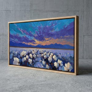 May include: A rectangular canvas print featuring an oil painting of a field of white cotton blossoms under a vibrant sunset sky with deep blue and purple clouds, framed in a light-colored wooden border, displayed at an angled perspective.