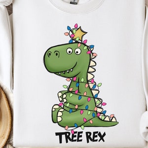 May include: White sweatshirt featuring a green dinosaur adorned with Christmas lights and a star on top. The text "TREE REX" is printed beneath the dinosaur.