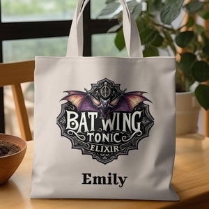 May include: White canvas tote bag with a black and purple bat wing design. The design includes the text "Bat Wing Tonic Elixir" and the name "Emily" is printed below the design.