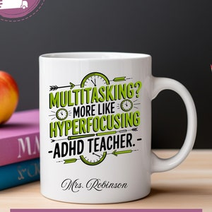 May include: White ceramic coffee mug with green text that reads "Multitasking? More like Hyperfocusing - ADHD Teacher."  The text is surrounded by clock faces and arrows. The mug also has the name "Mrs. Robinson" printed on it.
