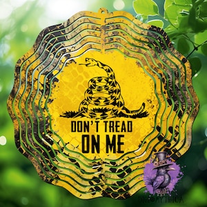 May include: A yellow metal wind spinner with a black rattlesnake and the words "Don't Tread On Me". The spinner has a distressed, weathered look.