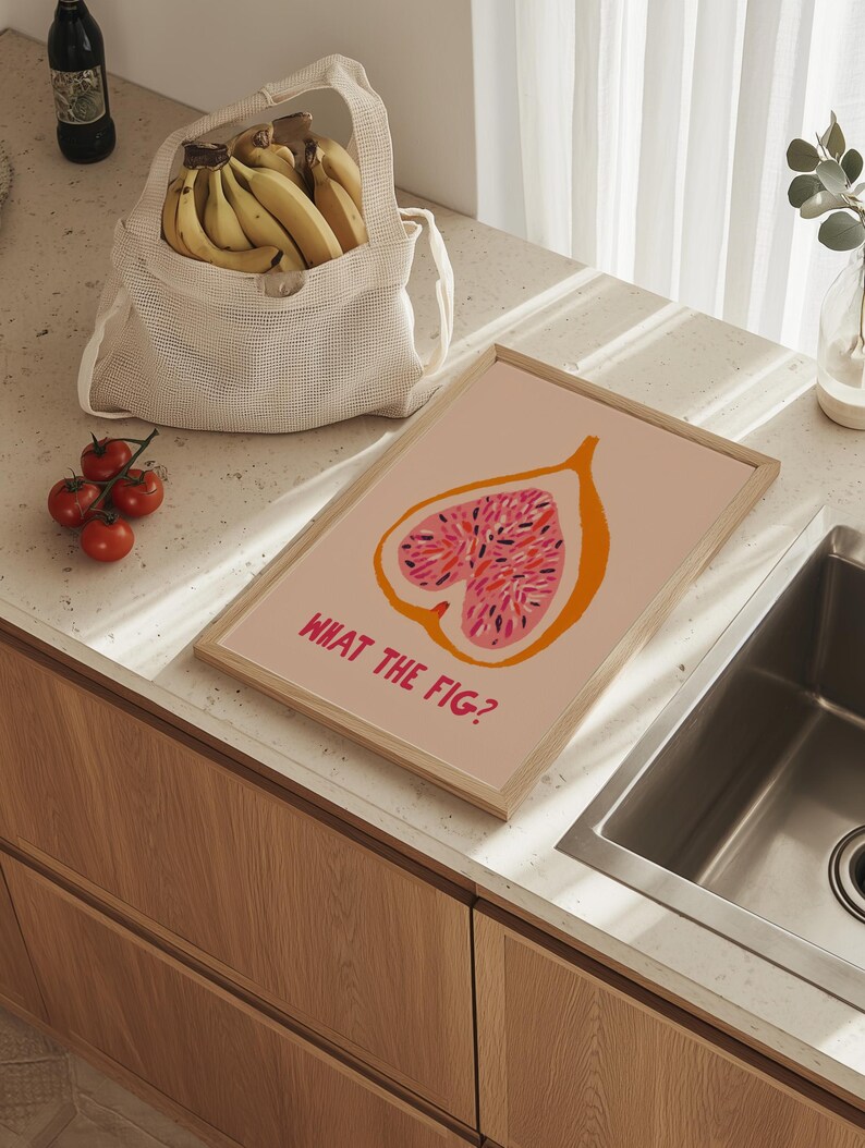Pu&ograve; includere: Una stampa artistica incorniciata con un'illustrazione di fico e la scritta "WHAT THE FIG?" in rosa. La stampa ha un contorno arancione su sfondo rosa chiaro. Sono visibili anche un sacchetto a rete pieno di banane e un grappolo di pomodori.