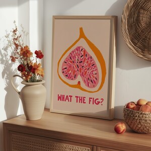 Pu&ograve; includere: Una stampa artistica incorniciata con un'illustrazione stilizzata di un fico tagliato, che mostra un interno rosa con semi colorati su sfondo pesca. La frase "WHAT THE FIG?" &egrave; stampata in rosa sotto.