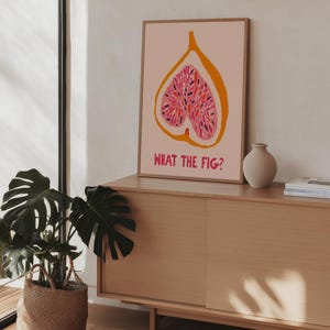 Pu&ograve; includere: Una stampa artistica incorniciata con un'illustrazione stilizzata di fico nei toni del rosa e dell'arancione, con la scritta "WHAT THE FIG?" in rosa. L'opera &egrave; esposta su un mobile in legno chiaro, con una pianta in vaso e un vaso.